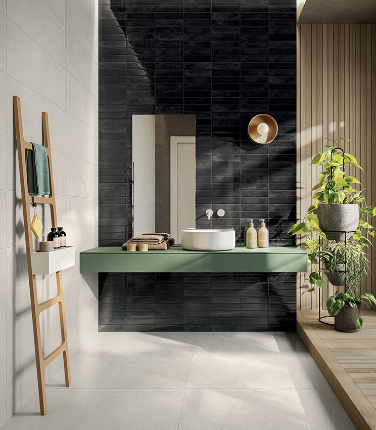 Modernes Badezimmer mit Oberflächen aus den Kollektionen La Matière Talc und Workshop Core, mit einer dunkel glänzenden Wand, hellen Flächen, einem schwebenden grünen Waschtisch, Holzelementen und zahlreichen Pflanzen im natürlichen Licht.