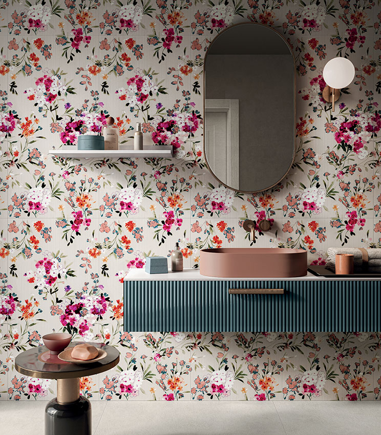 Modernes Badezimmer mit dekorativer Wandverkleidung aus der Kollektion Glam Bouquet, mit mehrfarbigem Blumenmuster auf hellem Hintergrund, schwebendem Waschtisch in Petrolblau, altrosa Waschbecken, großem ovalem Spiegel und abgestimmten Details in warmen Farbtönen.