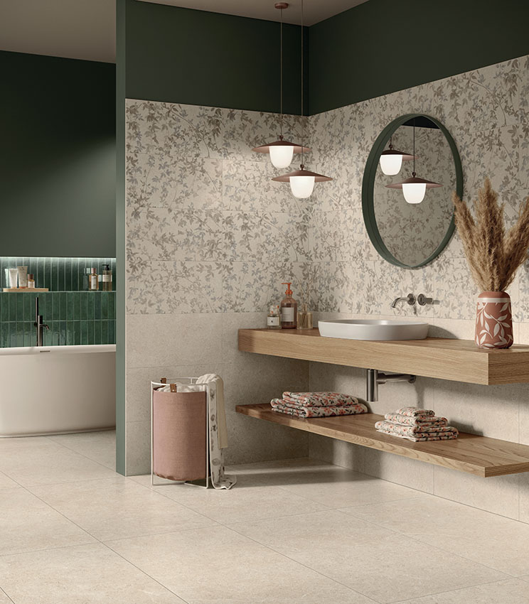 Modernes Badezimmer mit Oberflächen aus den Kollektionen Surround Sketch, Sketch Impressions, Sketch Soft und Workshop Jade, mit floralen Wandbelägen in neutralen Farbtönen, dunkelgrünen Wänden, einem weißen Waschbecken auf einer Holzablage, rundem Spiegel und einer freistehenden Badewanne im Hintergrund.