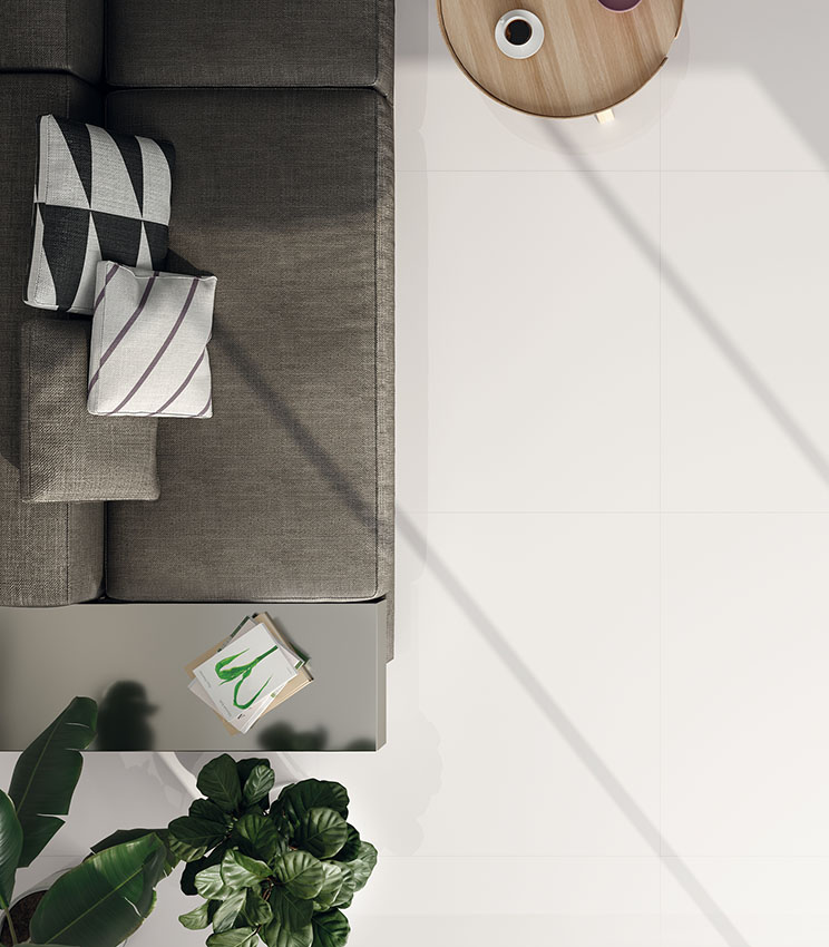 Draufsicht auf ein modernes Wohnzimmer mit grauem Sofa, rundem Couchtisch aus hellem Holz und glänzendem Boden in weißer Marmoroptik.