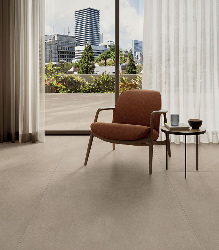 Blick in ein modernes Wohnzimmer mit Sessel und Schiebetür zu einer Terrasse mit Blick auf die Stadt. Boden in Betonoptik von Panaria Ceramica, Kollektion La Matière.
