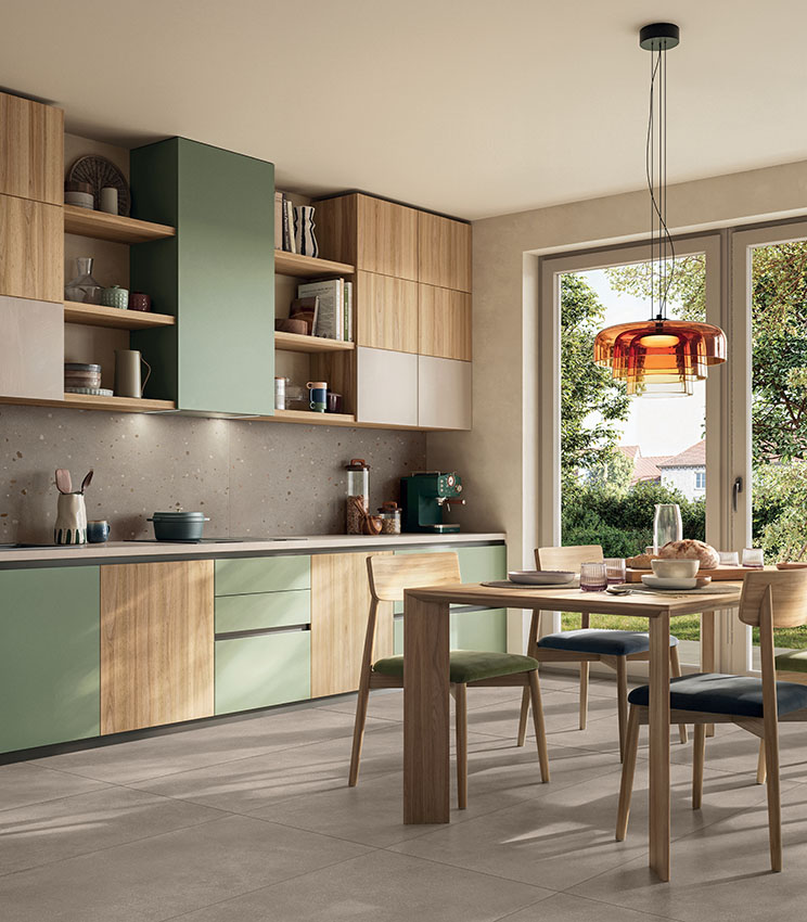 Moderne und einladende Küche mit Holz- und salbeigrünen Möbeln, hellem Essbereich und Feinsteinzeugboden in warmer Betonoptik.