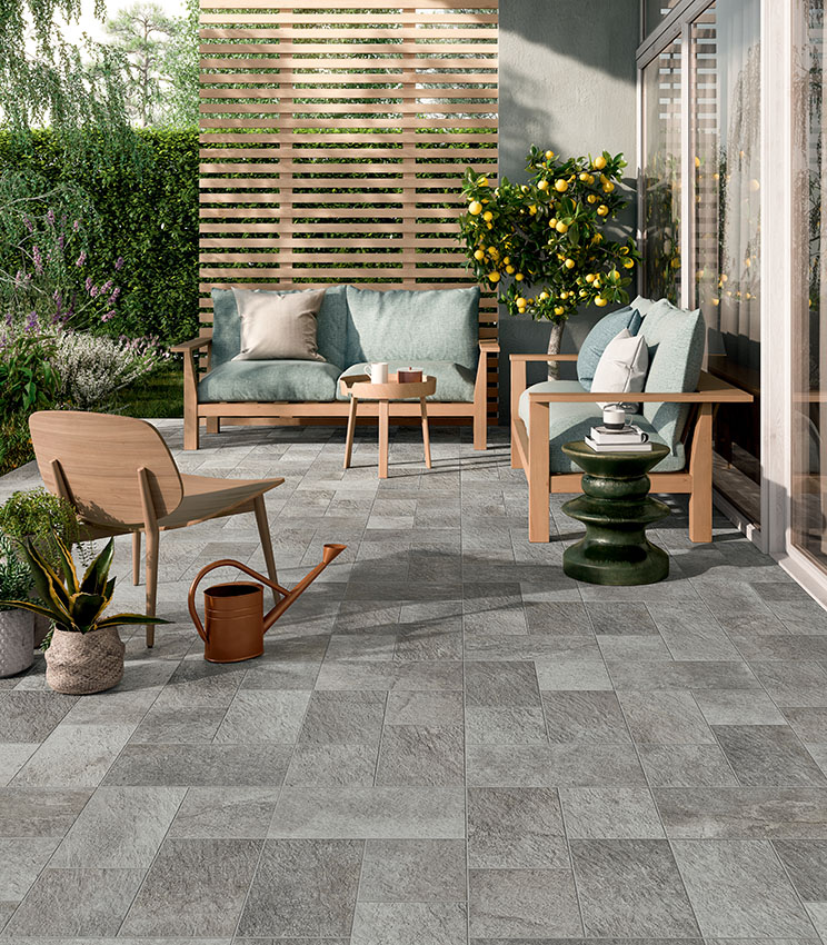 Moderne Terrasse mit Bodenbelag aus der Kollektion Pierre des Rêves Nuage, geprägt von grauen Oberflächen in Steinoptik in modularen Formaten. Der Bereich ist mit Sofas und Sesseln aus Holz, salbeigrünen Kissen, dekorativen Beistelltischen, Topfpflanzen und einem Zitrusbaum inmitten üppiger Vegetation eingerichtet.