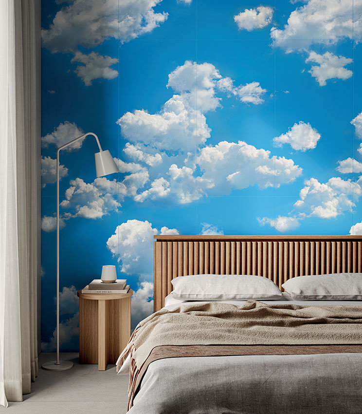 Modernes Schlafzimmer mit dekorativer Wandverkleidung aus der Kollektion Glam Flow, die einen blauen Himmel mit großen weißen Wolken zeigt. Der Raum ist mit einem Bett mit geriffeltem Kopfteil aus Holz, Bettwäsche in neutralen Farbtönen, einem Nachttisch aus Holz und einer weißen Stehleuchte eingerichtet.