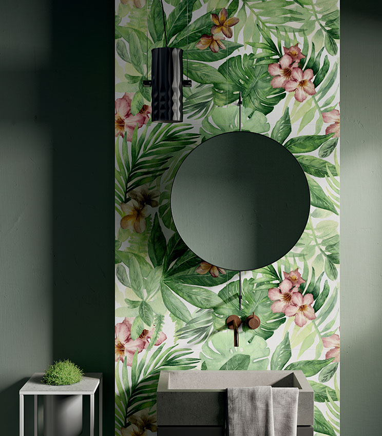 Modernes Badezimmer mit dekorativer Wandverkleidung aus der Kollektion Glam Rainforest, geprägt von einem tropischen Muster mit großen grünen Blättern und rosa Blüten. Der Raum verfügt über dunkelgrüne Wände, ein kantiges Waschbecken, einen runden Spiegel, wandmontierte Armaturen und eine schwarze Pendelleuchte.