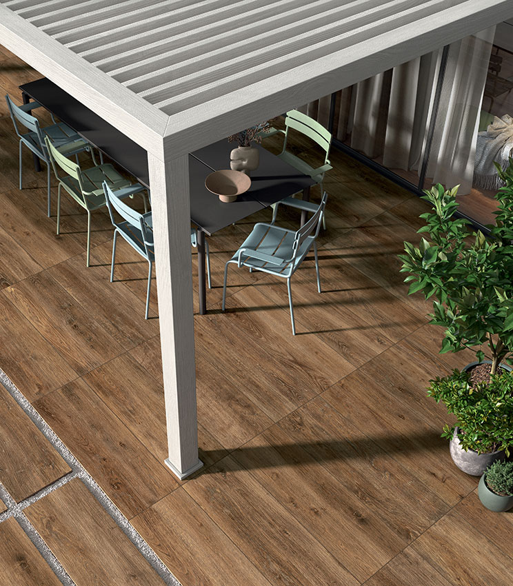 Außenbereich mit Feinsteinzeugboden in Holzoptik, modernen Möbeln und Pergola für ein einladendes, widerstandsfähiges und natürlich wirkendes Ambiente.
