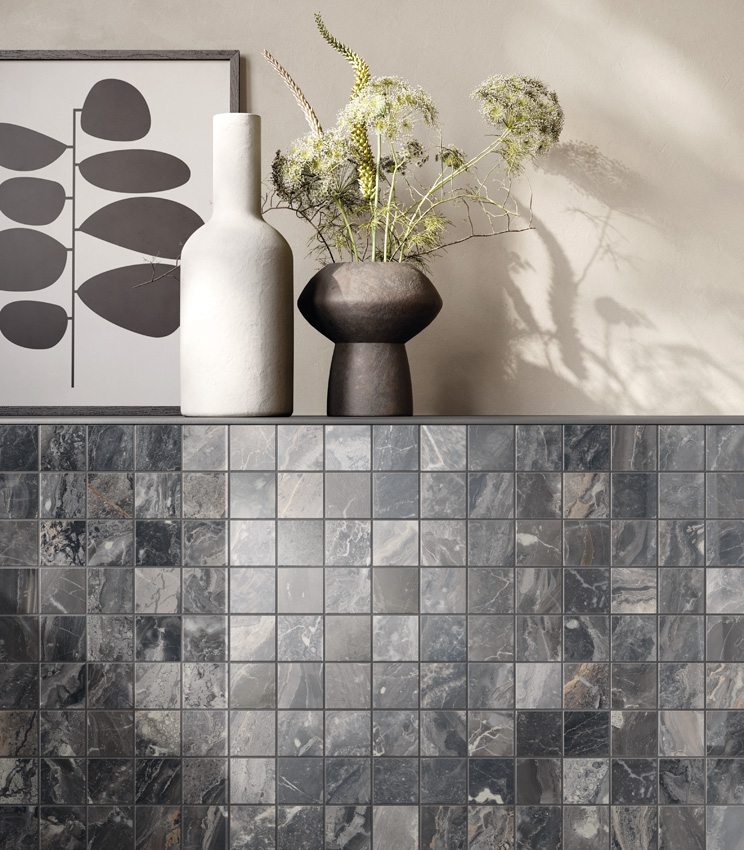 Nahaufnahme einer Frontansicht einer niedrigen Mauer mit einem Regal, auf dem zwei Vasen und ein abstraktes Gemälde stehen. Die niedrige Mauer ist mit dunklem Marmor-Optik-Keramikmosaik verkleidet, während der Rest der Wand in Elfenbein gestrichen ist.