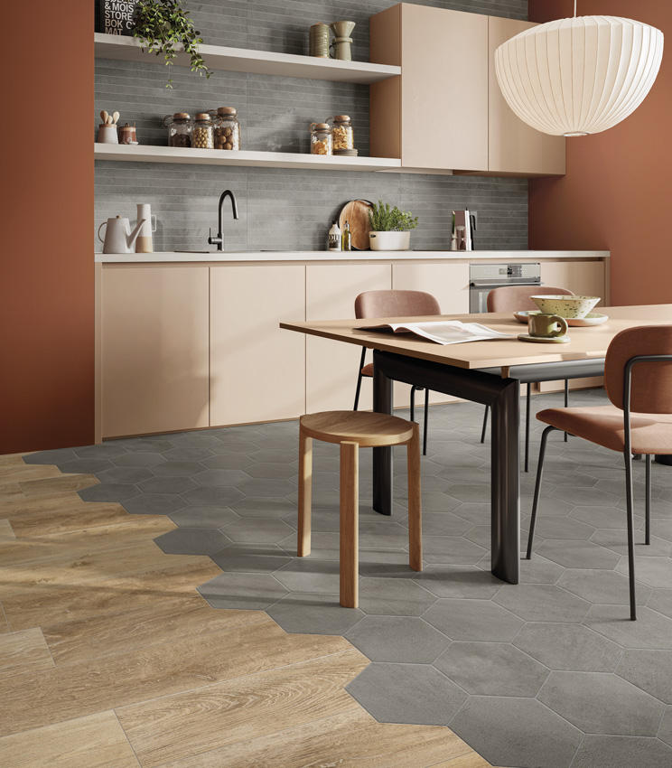 Blick in eine moderne Küche mit ziegelrot gestrichenen Wänden und puderrosa Möbeln, einer Küchenrückwand aus grauen Beton-Optik-Feinsteinzeug-Leisten und einem Mehrefekt-Boden aus keramischen Beton-Sechseckfliesen und Holzoptik-Feinsteinzeug-Dielen.