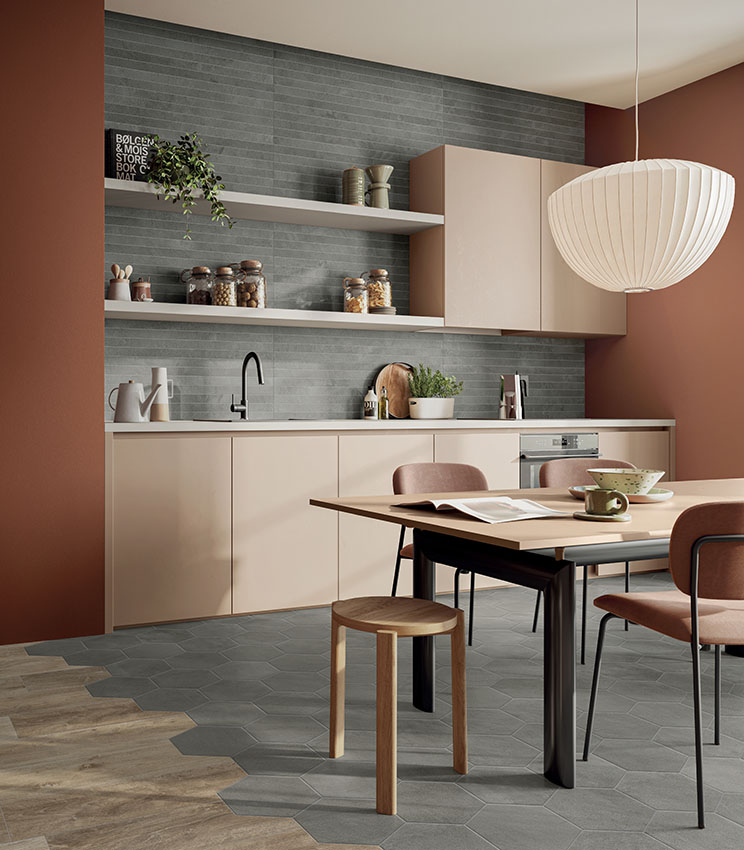 Moderne Küche mit grauem Wandbelag in linearer Optik und geometrischem Boden, eingerichtet mit beigefarbenen Küchenmöbeln, terrakottafarbenen Wänden, einem Esstisch mit gepolsterten Stühlen und einer großen weißen Pendelleuchte.