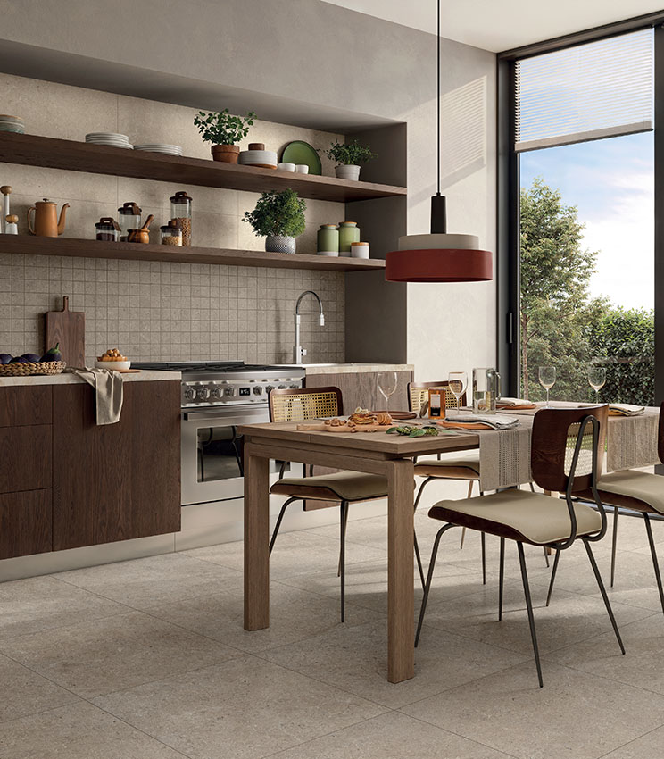 Moderne Küche mit beigefarbenen Boden- und Wandfliesen in Steinoptik, Holzmöbeln, Esstisch und großem Fenster.