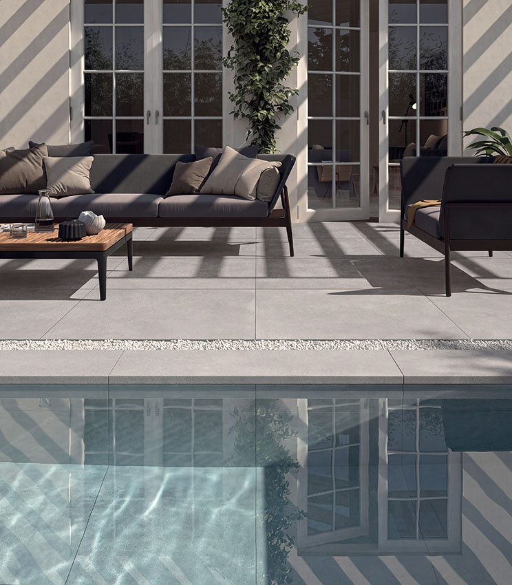 Poolbereich mit Feinsteinzeugboden in Betonoptik, modernen Outdoor-Möbeln und großen Fensterflächen für ein elegantes und funktionales Ambiente.